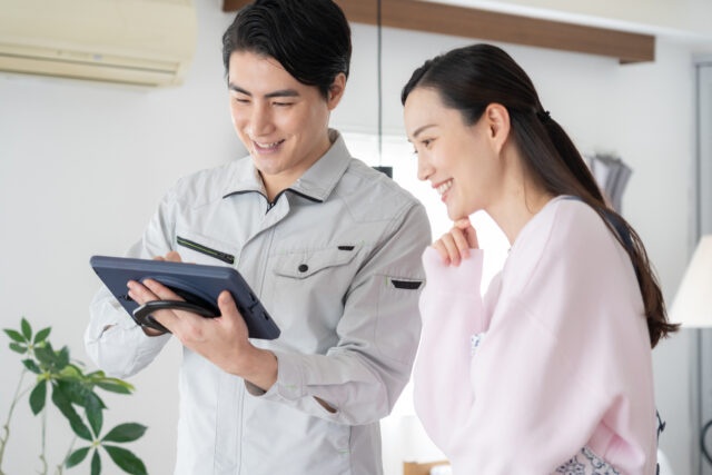 タブレットを見ながらエアコンについて相談する女性と担当者